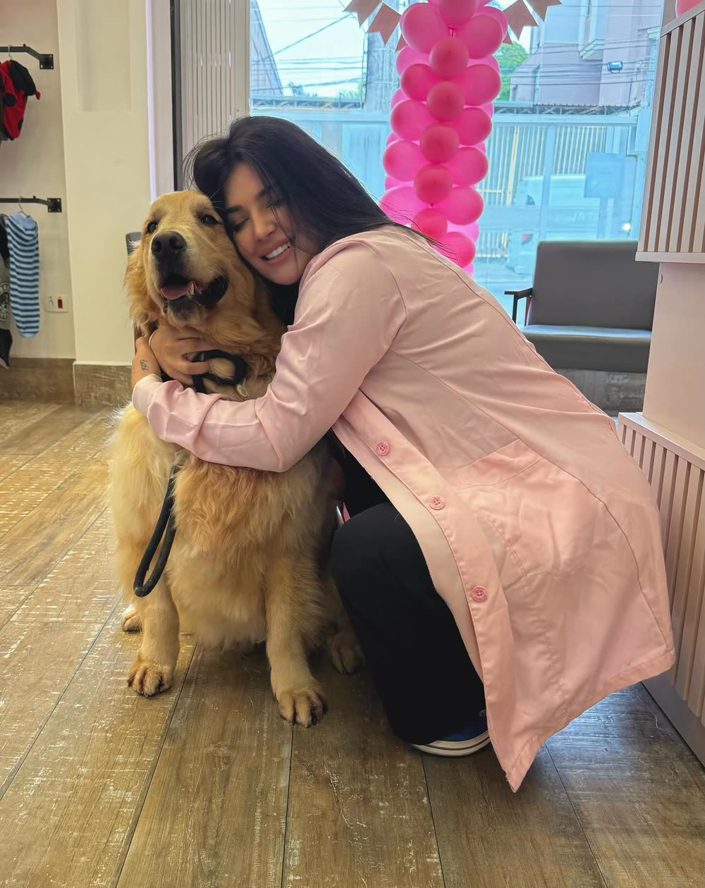 Dra. Rebecca de jaleco rosa abraçando o Chico, um golden retriever