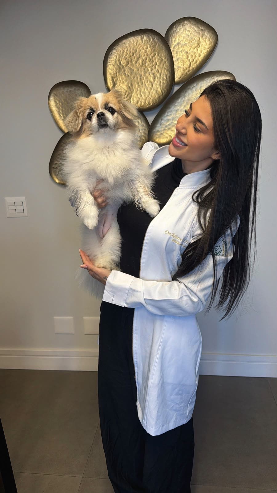 Dra. Rebecca de jaleco branco com um cachorrinho de pelo longo no colo
